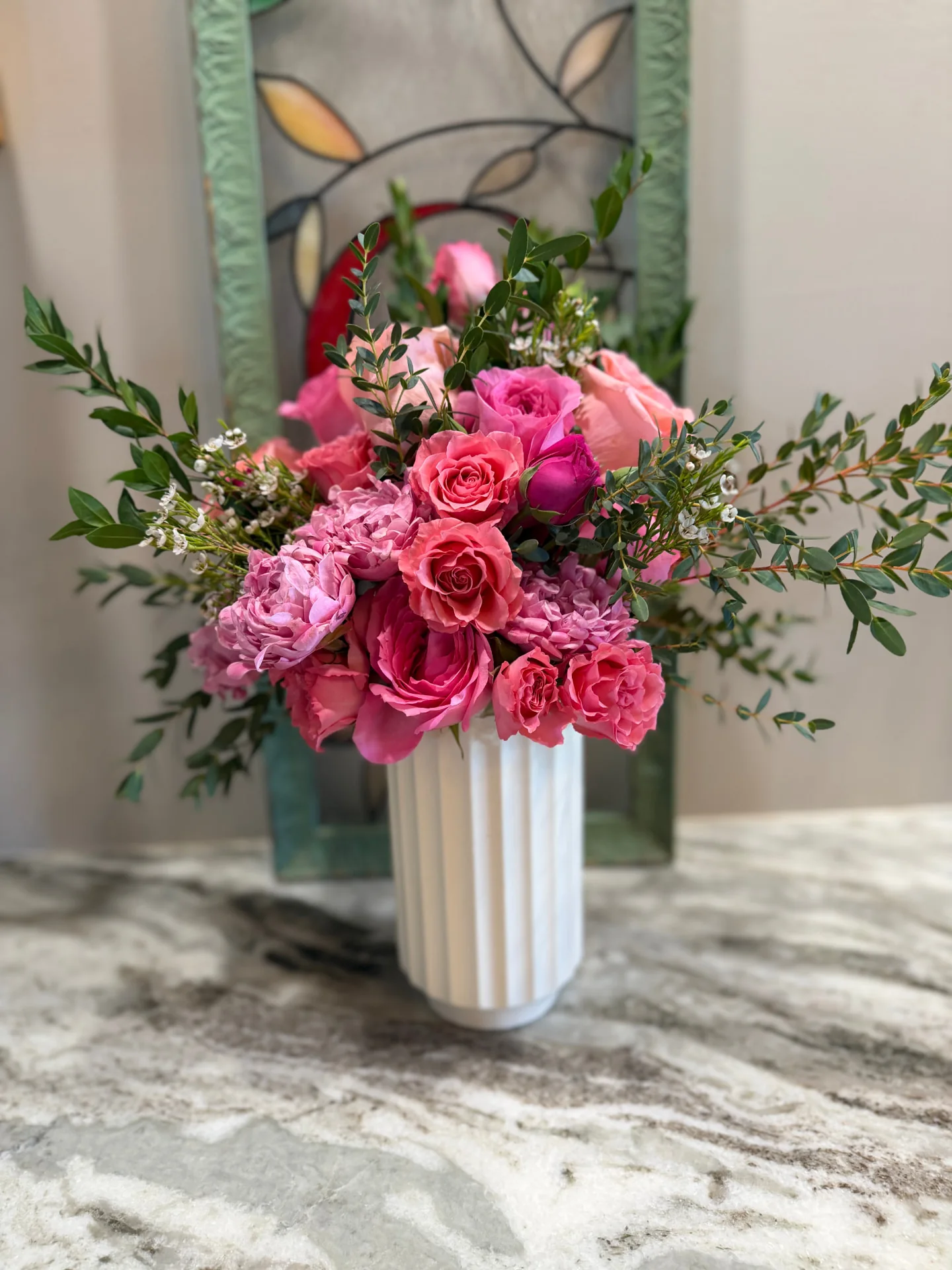 Pink garden roses, peonies and eucalyptus in a white fluted vase